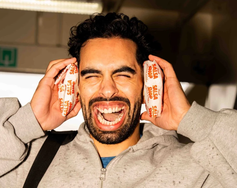 Student making a funny face while holding two Salsa Shop quesadillas to his ears during a student activation event, showing playful and youthful brand engagement.