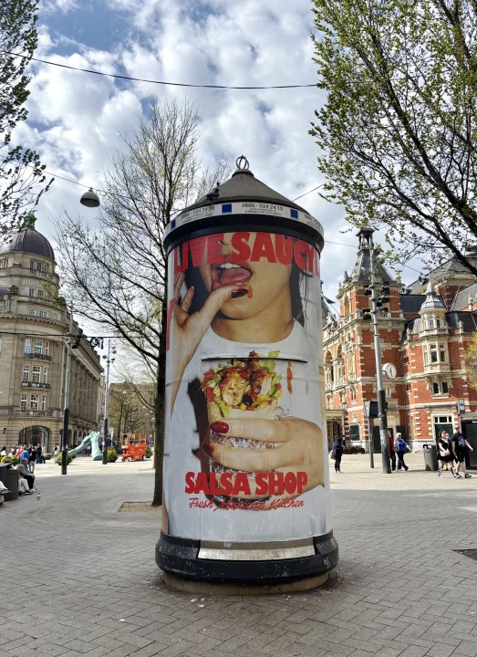 Salsa Shop Live Saucy out-of-home campaign displayed on a large advertising pillar in central Amsterdam, featuring bold campaign photography and a Salsa Shop burrito.